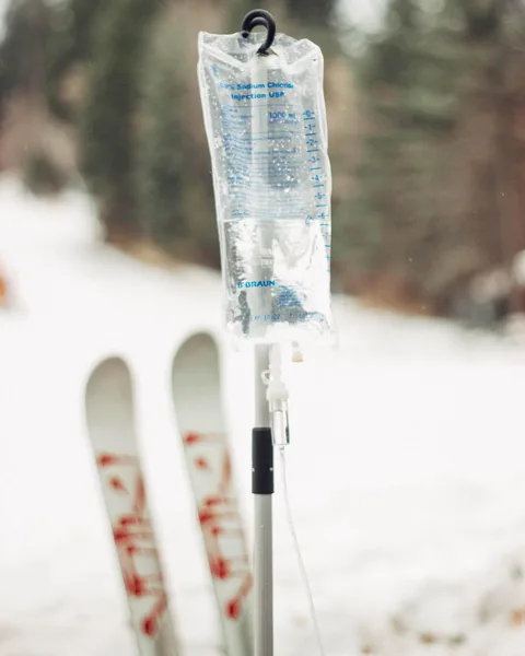 An IV pole standing in the snow beside a pair of skis