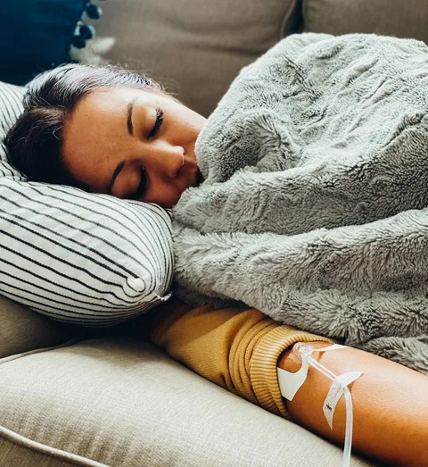 A woman asleep in bed under a grey blanket during her IV