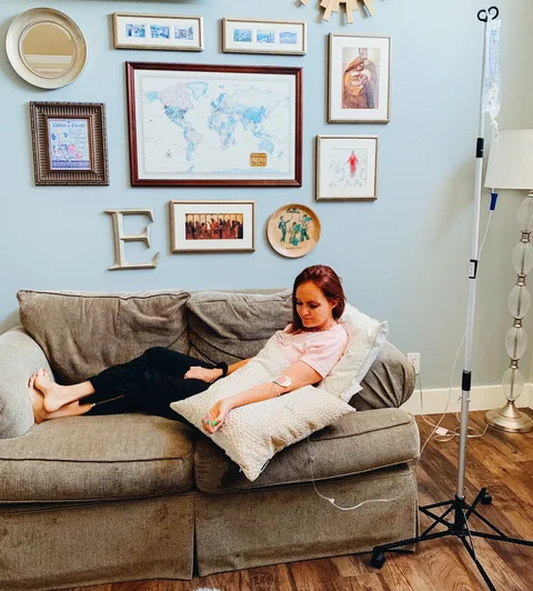 A woman resting on her couch during her IV, her IV pole beside her