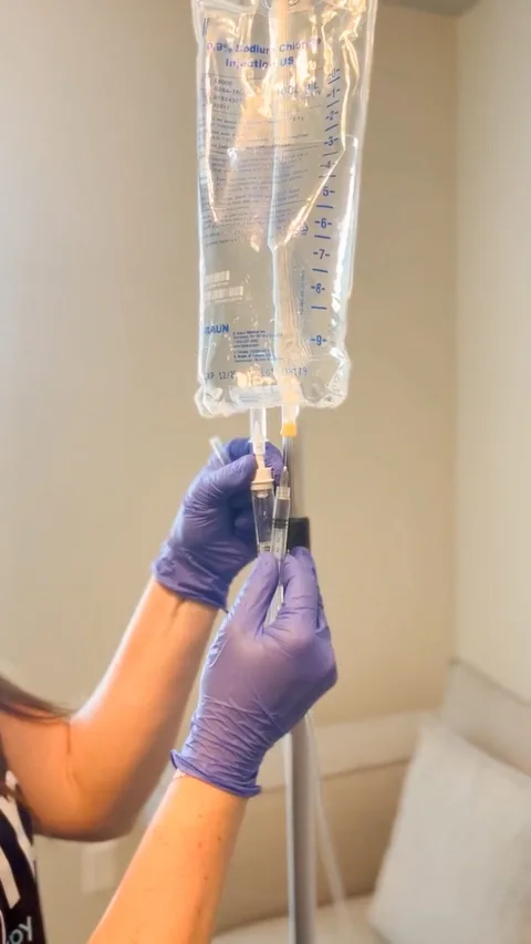 A nurse's gloved hands adding to an IV bag