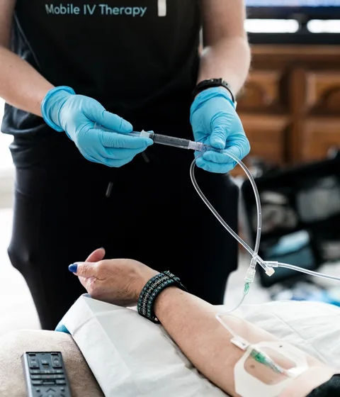 A DrpIV+ nurse's gloved hands setting up a client's IV line