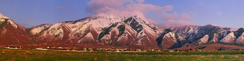 Elk Ridge homes at the foot of snow-covered mountains, lit pink at sunset
