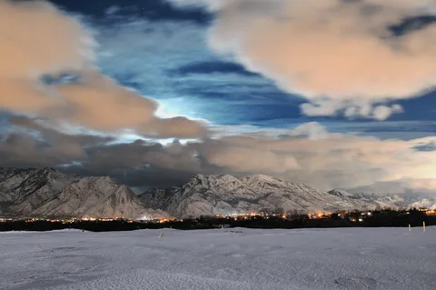 Snowy Wasatch peaks above the lights of Highland on a moonlit winter night