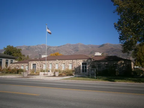 Kaysville's old stone city hall with the Wasatch Mountains behind it under a blue sky