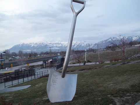 Giant shovel sculptures at Roy's FrontRunner station with the snowy Wasatch Mountains behind