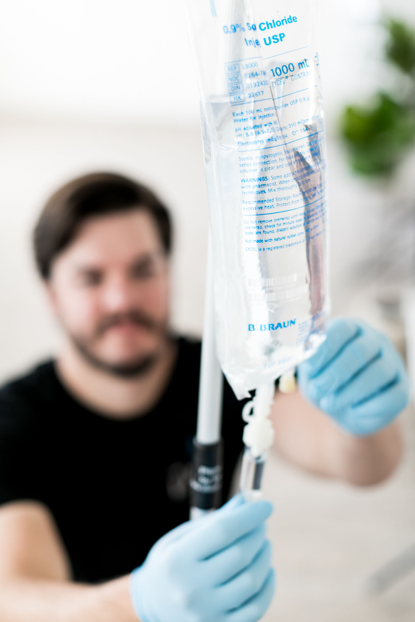 Male nurse in the background holding up a bag of saline