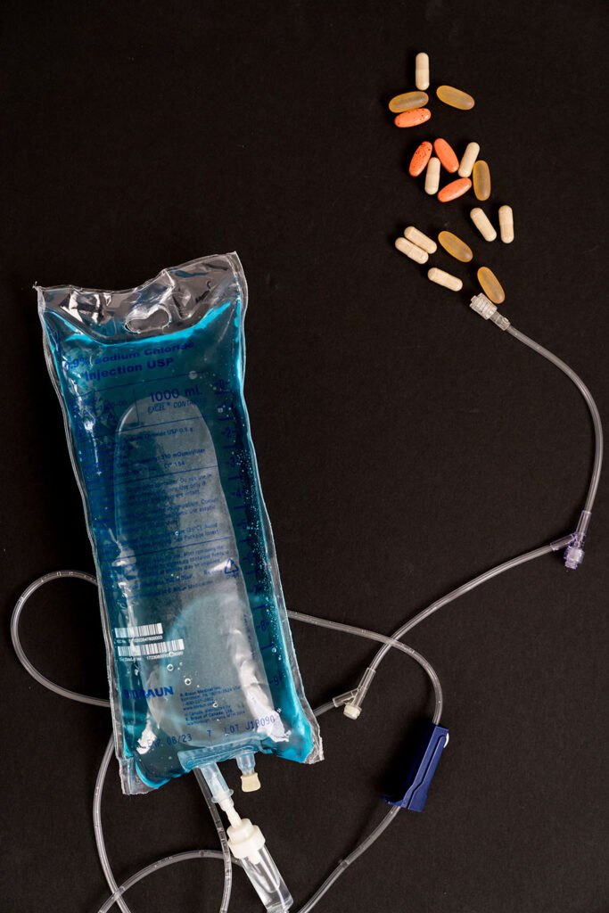 IV Bag with blue fluids against a black background with vitamins splayed on table