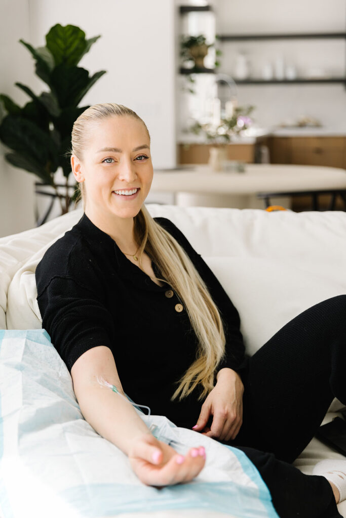 Smiling woman getting IV therapy at home on a white couch