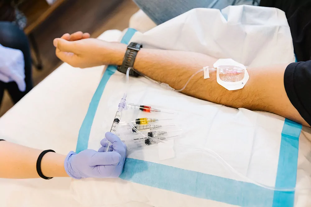 Close up of a man getting an IV as the nurse is pushing vitamins into the IV