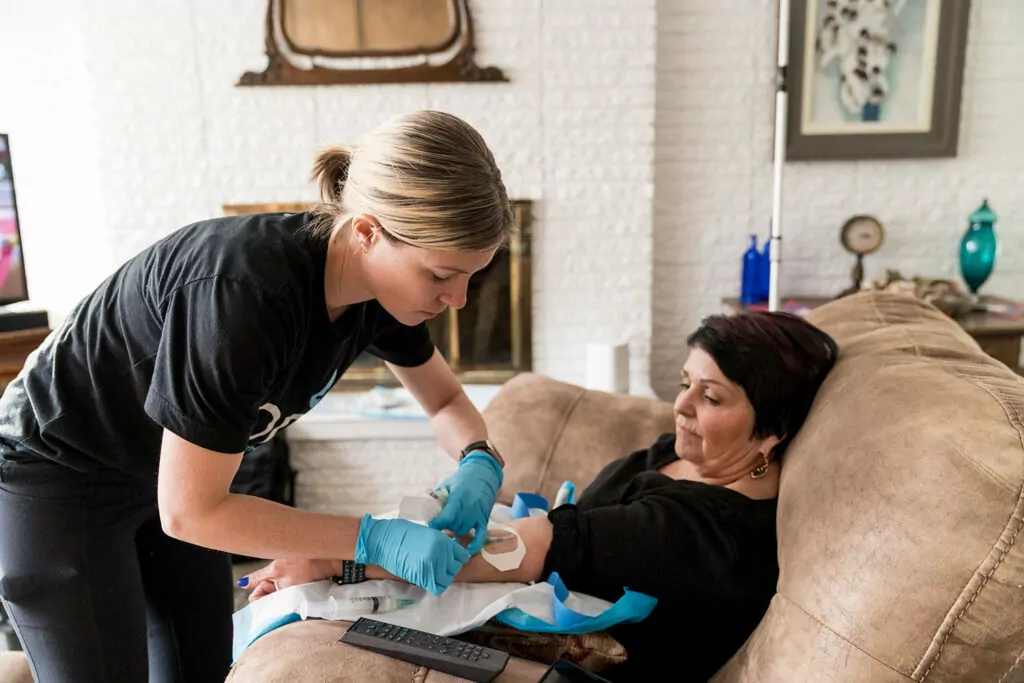 Woman sitting on a recliner getting migraine infusion therapy from a Drp IV nurse doing IV drip therapy