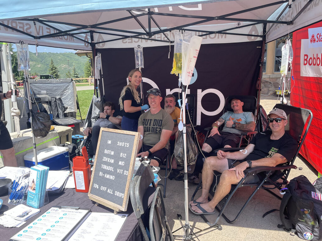 A group of spartan athletes getting IV therapy in a drip iv event tent and a bunch of IV fluid bags hanging on poles