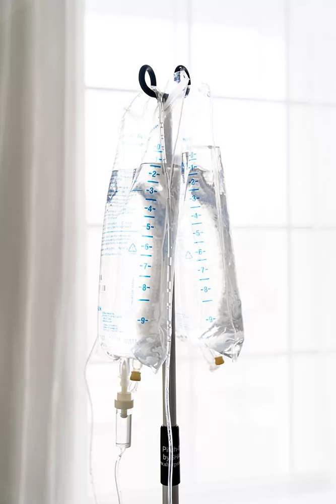 IV fluids hanging on a pole against a window background to represent how long the benefits of iv fluids last