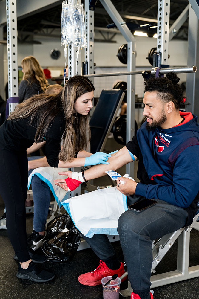 Nurse doing Mobile IV Therapy in South Jordan for a man in a gym sitting under a squat rack