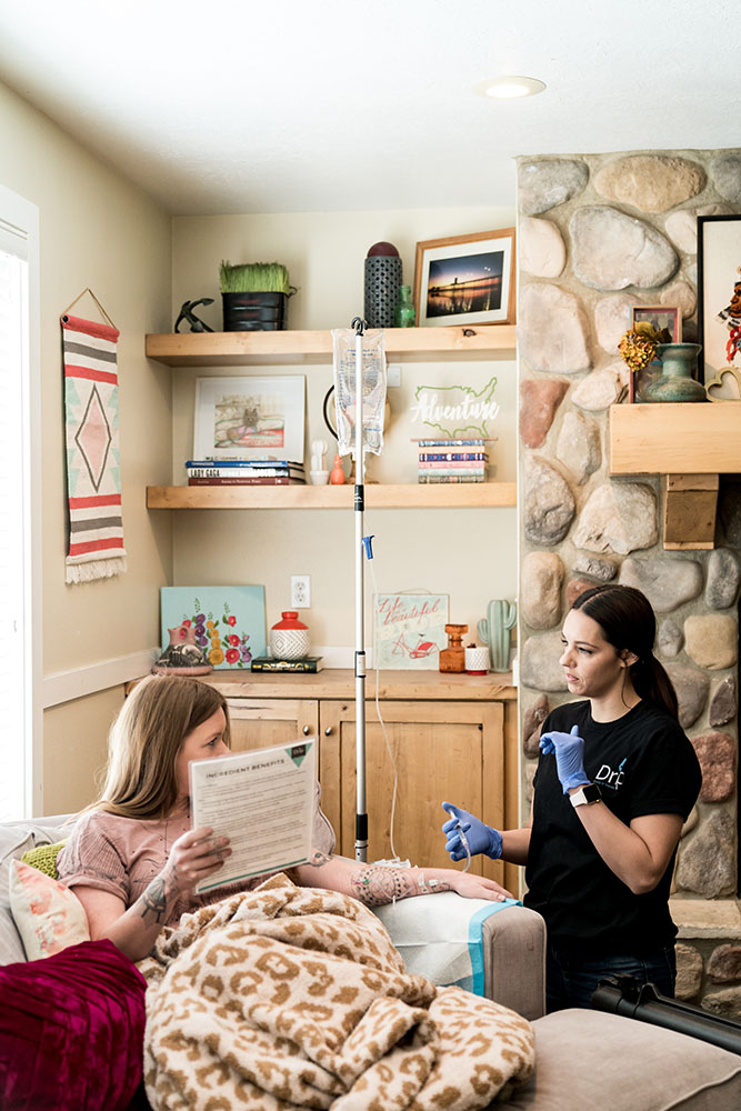 A Nurse explains what an IV for sickness is to a patient sitting on a couch with a blanket