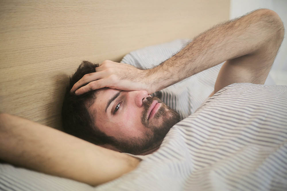 man lying in bed with hand on face wondering how to get rid of hangxiety