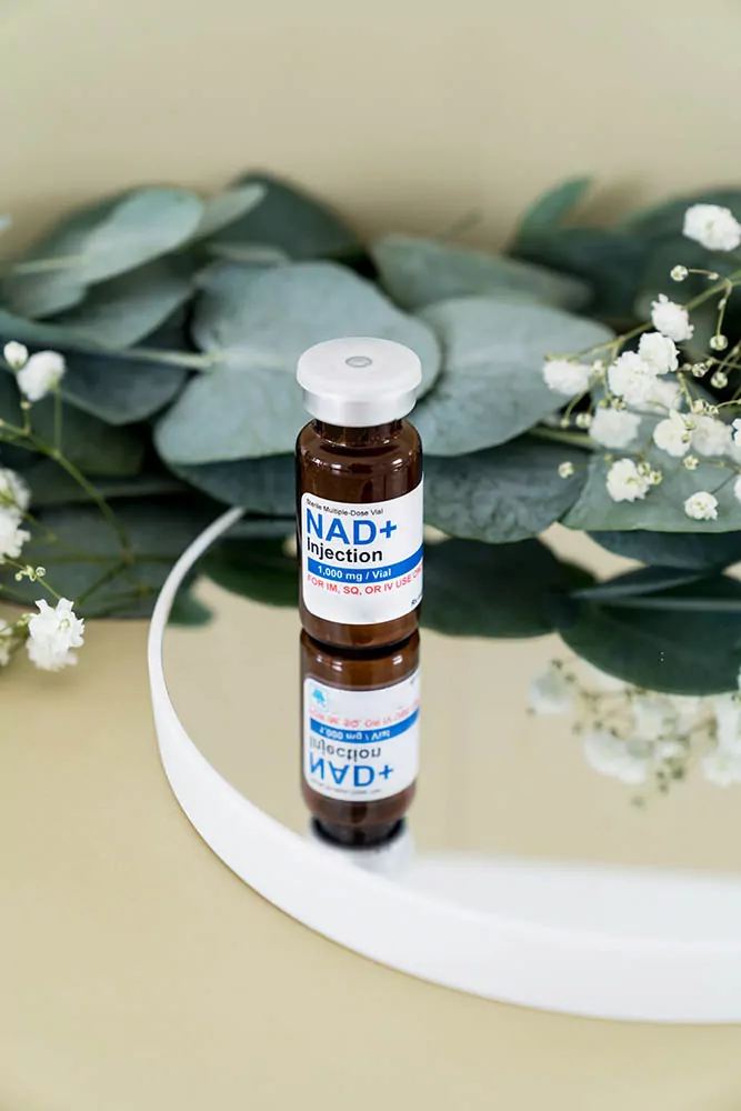A vial with NAD+ IV therapy Dosage on a reflective surface and greenery in the background