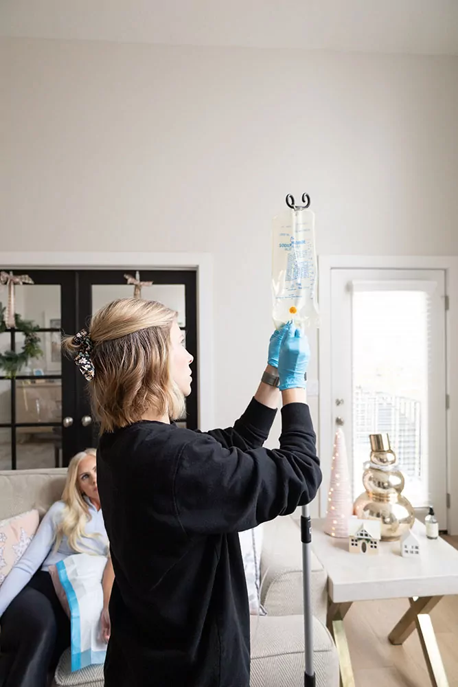 nurse explaining the benefits of glutathione iv therapy while prepping an IV bag. The patient sitting in the background on a couch.